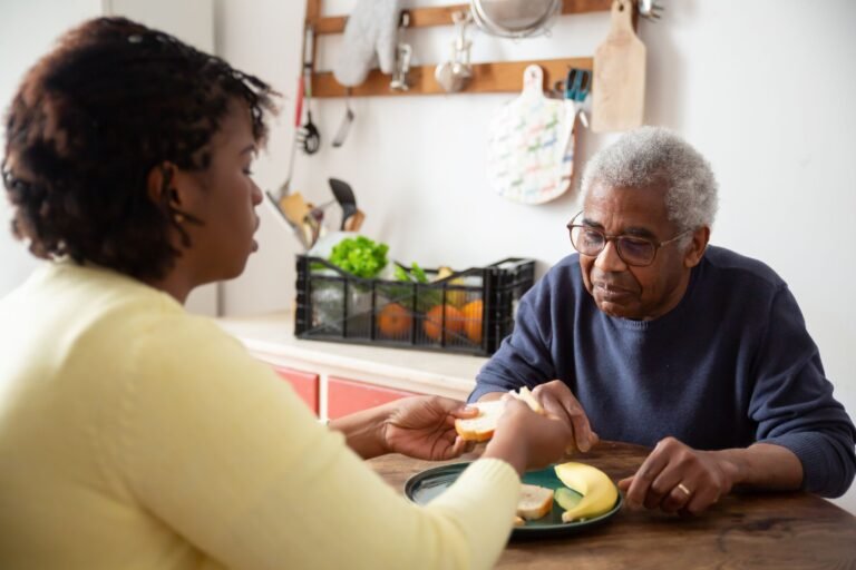 Une aidante aide un homme âgé, qui semble peu manger, lors d'un repas à domicile