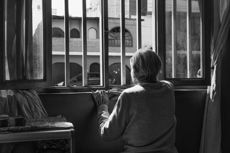 Femme âgée assise seule, regardant pensivement par la fenêtre de son domicile