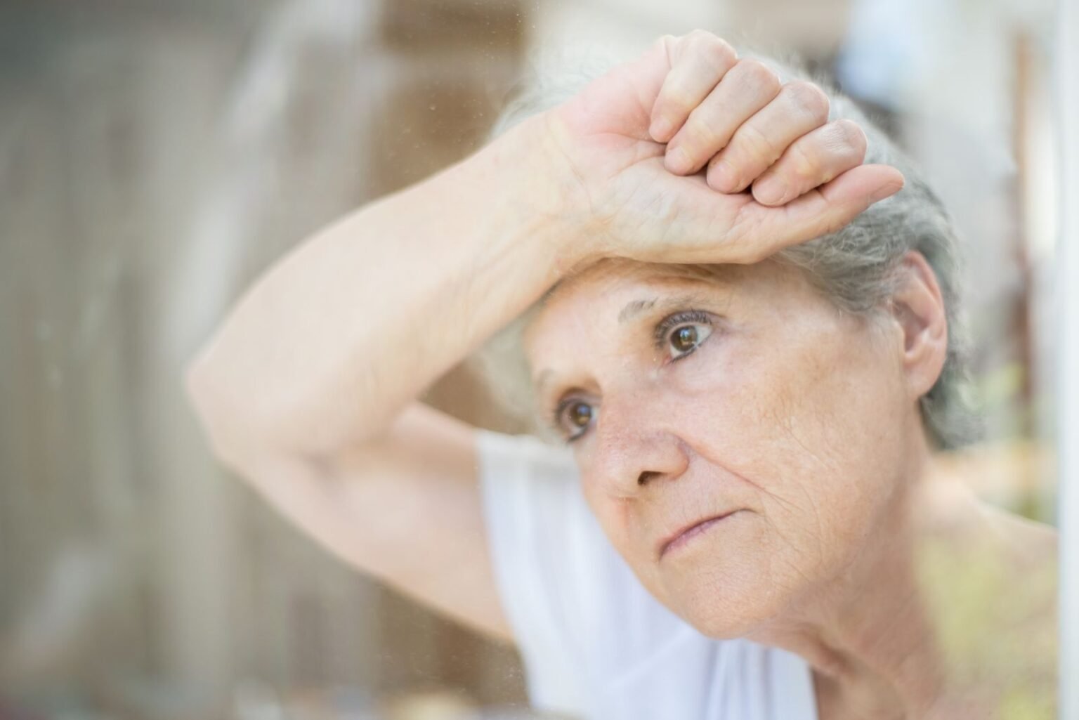 Femme âgée au regard las, appuyée contre une fenêtre, image d'un proche qui semble se replier sur lui-même