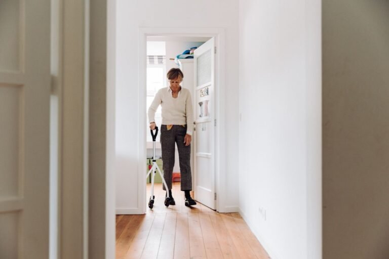 Femme âgée marchant dans le couloir de son logement avec une canne tripode, pour rester active malgré une sciatique